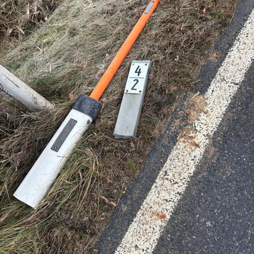 An orange and gray traffic sign with the number 42 is broken and lying on the grass near the road.