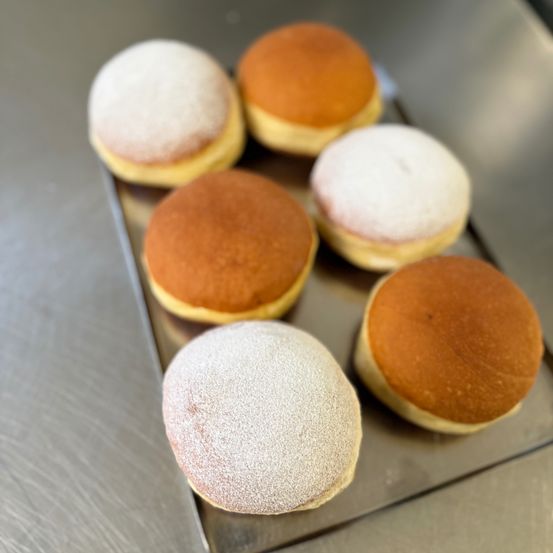 Ein Tablett hält sechs runde Brötchen mit Puderzucker auf einer Metalloberfläche. Sie sind braun und weiß mit verschiedenen Belägen.