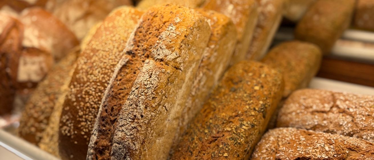 Eine Theke voller verschiedener Brotsorten, darunter Vollkorn- und Mehrkornbrote, wird von Deckenleuchten beleuchtet.