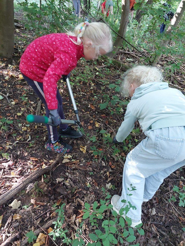 Zwei junge Mädchen buddeln im Wald im Schmutz, eine hält eine Schaufel und die andere benutzt ihre Hände.