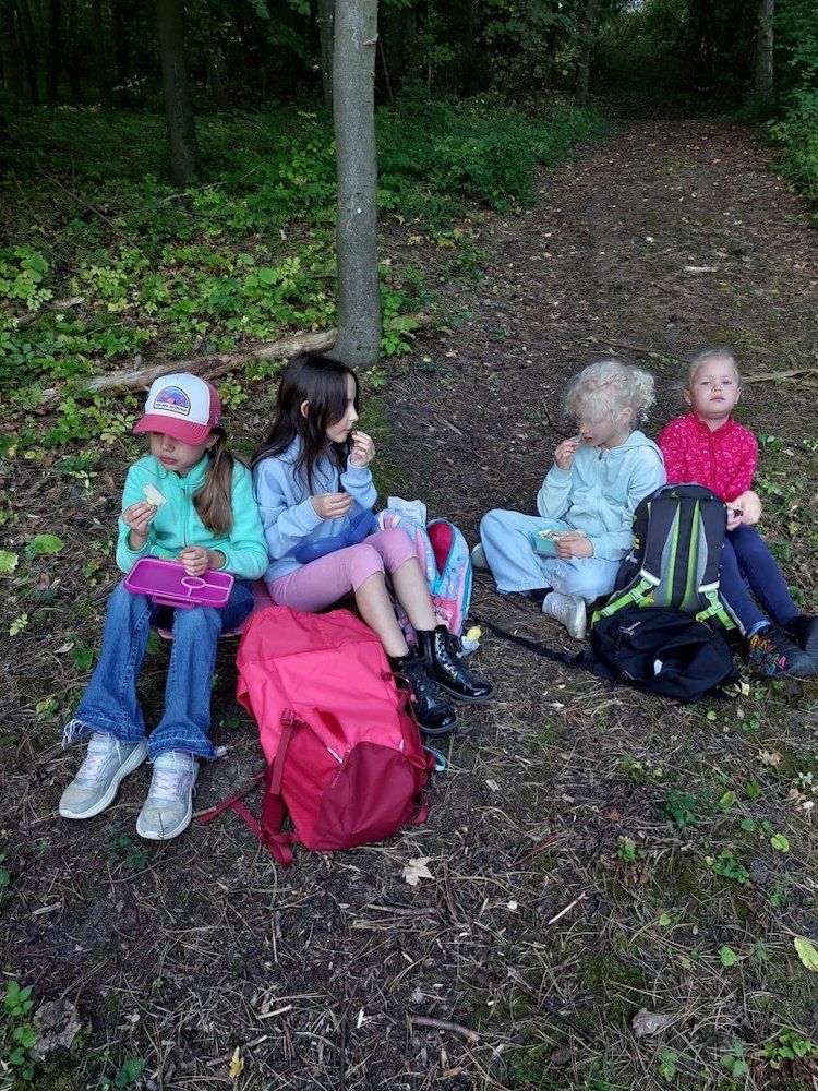 Fünf junge Mädchen sitzen auf dem Boden in einem Wald und essen.
