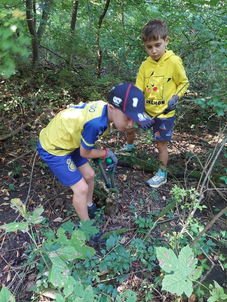 Zwei junge Jungen sind in einem Wald, einer hält einen Stock und der andere ein Werkzeug.