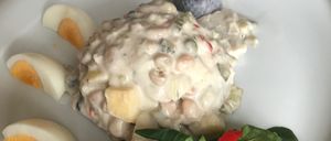 Ein weißer Teller enthält ein Gericht aus Fischsalat mit cremiger Textur, garniert mit geschnittenen gekochten Eiern und roten Paprikaschoten.