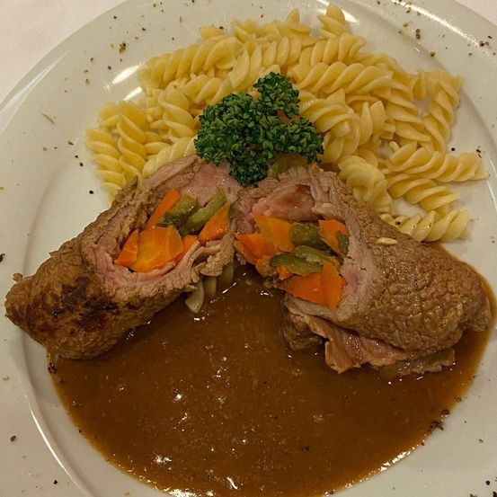 Ein Teller mit geschnittenem Fleisch, Gemüse und brauner Sauce, begleitet von einer Seite Pasta.