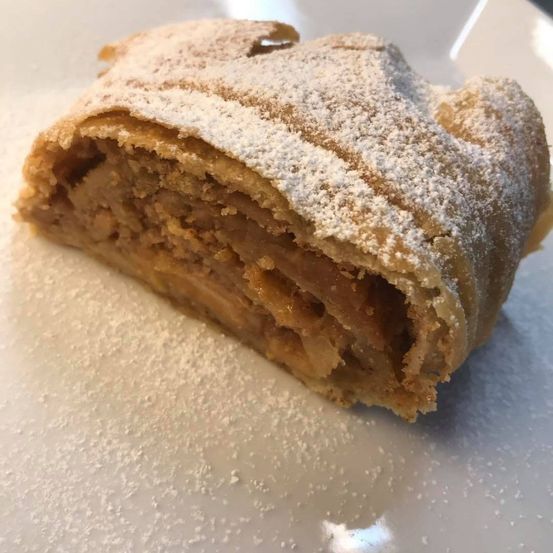 Ein Stück Apfelstrudel mit knuspriger Kruste und einer Füllung aus karamellisierten Äpfeln, bestreut mit Puderzucker.