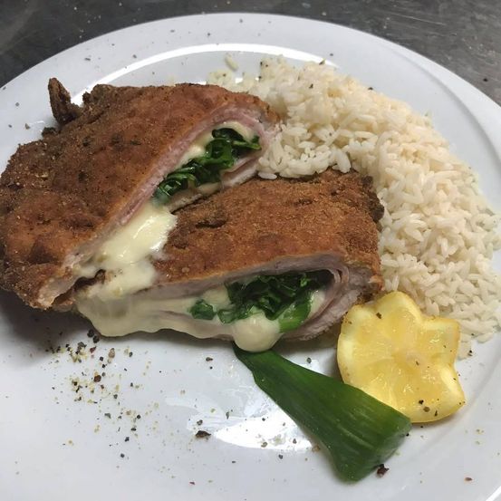 Ein Teller mit zwei panierten Hähnchenschnitzeln, geschmolzenem Käse und Spinat, begleitet von Reis und einer Zitronenscheibe.