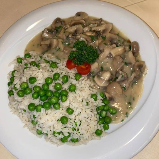Ein Teller mit Reis, grünen Erbsen und Pilzsoße, garniert mit einem Petersilienzweig und zwei Kirschtomaten.