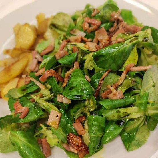 Ein Teller mit Spinatsalat, knusprigem Speck und goldenen Kartoffeln als Beilage.