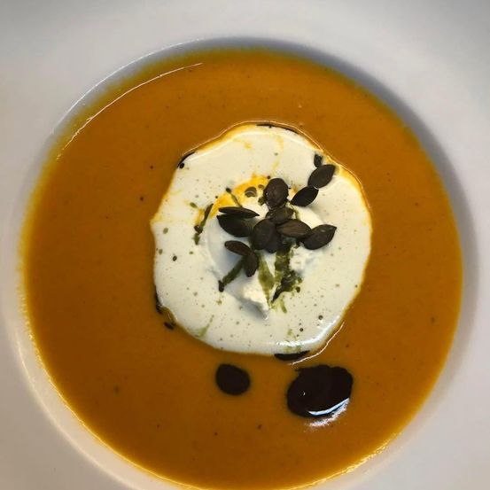 Eine Schüssel Kürbissuppe mit einem Klecks weißer Sahne und Kürbiskernen obenauf.
