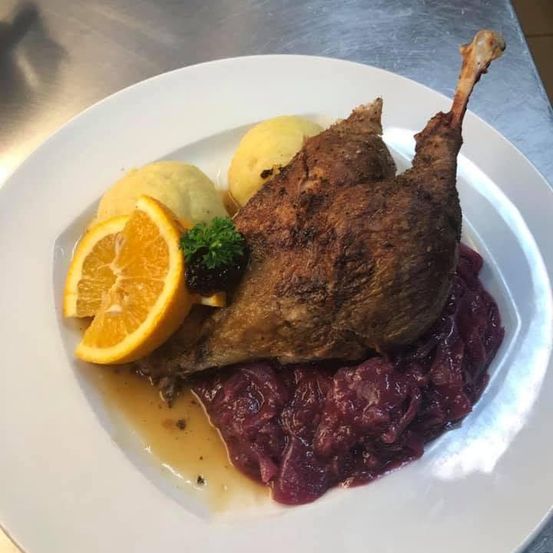 Ein Teller mit gebratener Ente, Rotkohl, Kartoffelpüree und einer Orangenscheibe auf einem weißen Teller.