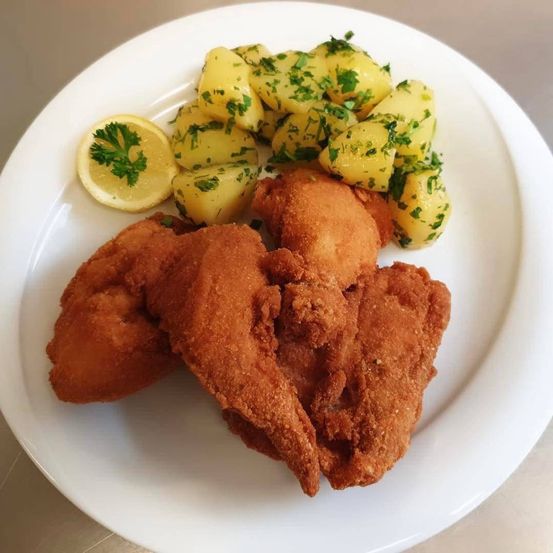 Ein weißer Teller mit gebratenen Fischstücken und einer Beilage aus Kartoffelpüree, garniert mit Petersilie und einer Zitronenscheibe.