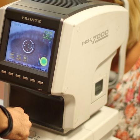 Eine Hand hält ein weißes HUITZ HRK 7000 Ophthalmoskop. Das Gerät zeigt eine digitale Anzeige einer Augenscannung.