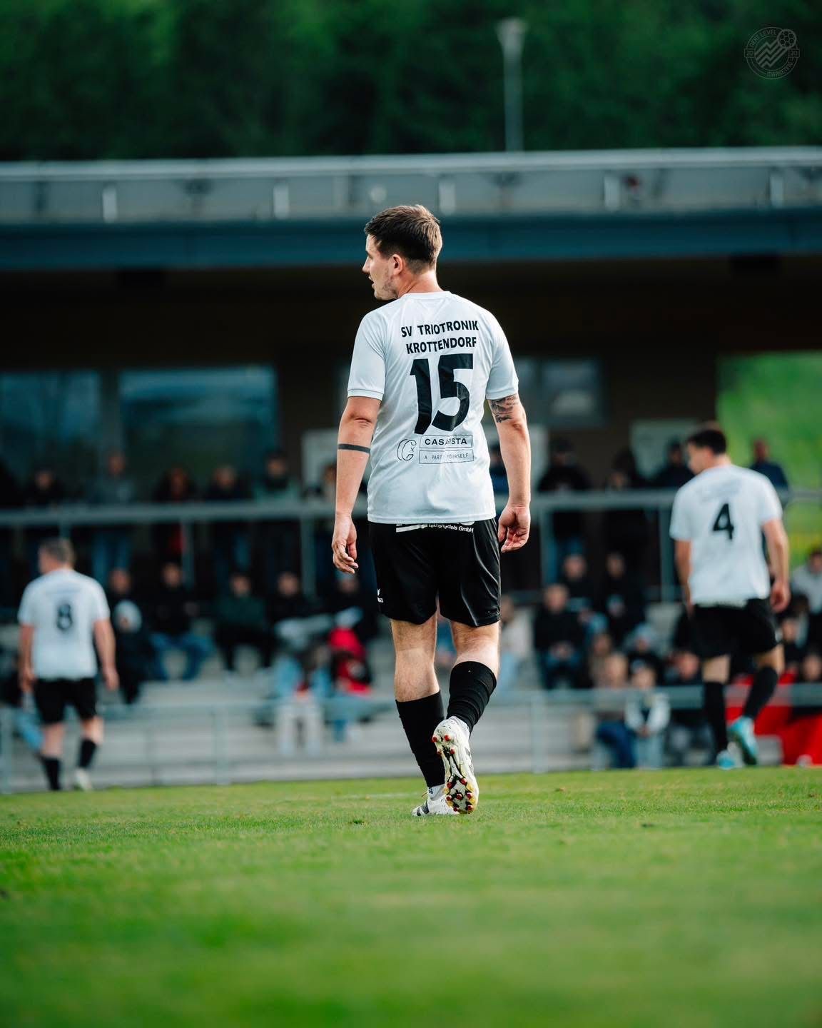 Ein Fußballspieler mit der Nummer 15 auf seinem Trikot läuft auf dem Spielfeld, während die Zuschauer im Hintergrund stehen.