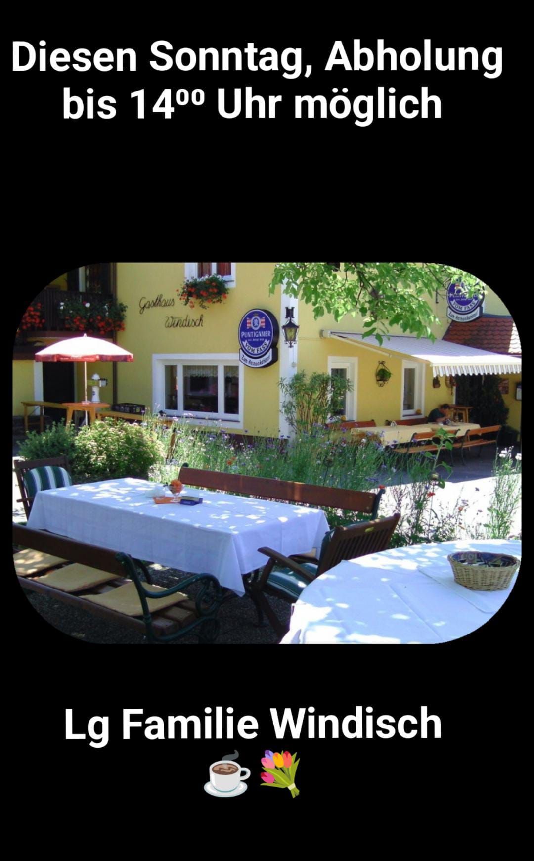 Außensitzplätze bei einem gelben Gebäude mit Tisch und Stühlen, einem Regenschirm und Pflanzen. Ein blaues Schild ist an der Wand.