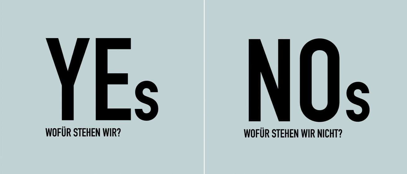 Das Bild zeigt zwei Seiten eines Posters, eine Seite hat die Buchstaben 'Es' in Schwarz auf blauem Hintergrund und die andere Seite hat 'Ns' mit einem Fragezeichen in Schwarz auf blauem Hintergrund.