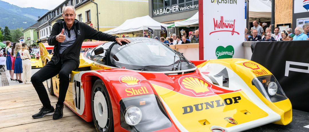 Ein älterer Mann sitzt auf einem roten und gelben Rennwagen mit dem Wort Shell darauf. Hinter ihm steht ein Gebäude mit dem Wort Habacher an der Seite.