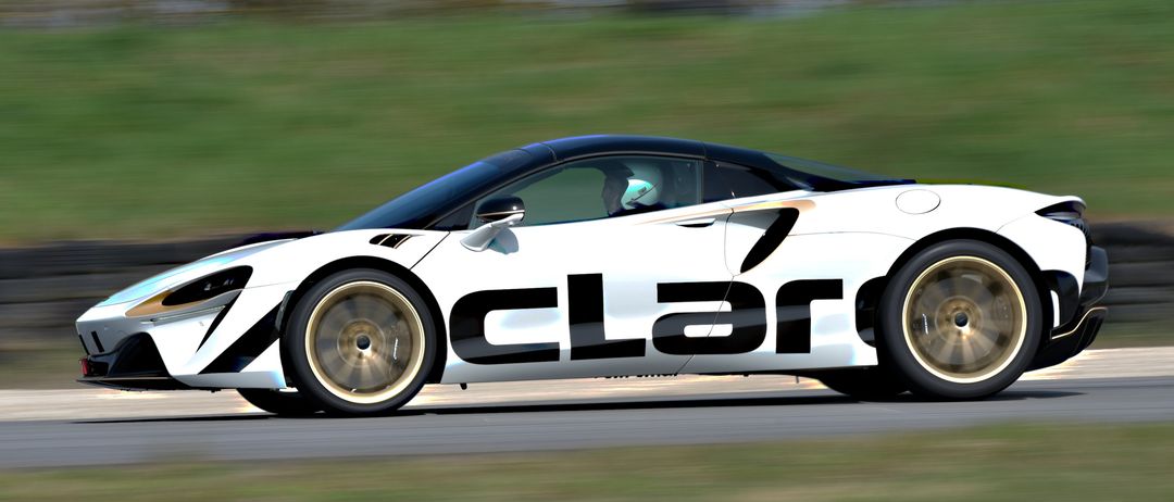 Ein weißer und schwarzer Sportwagen mit dem Wort 'CLAR' an der Seite, gefahren von einer Person mit Helm, ist auf einer Rennstrecke in Bewegung.