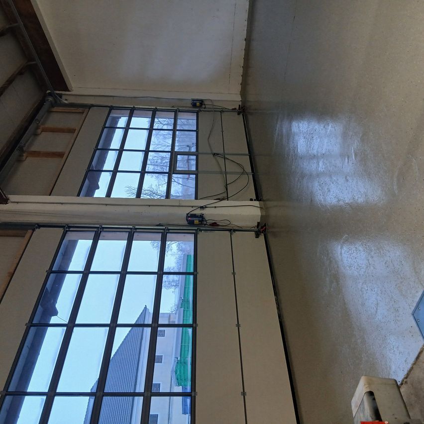 Ein Blick von unten auf eine Garage mit Glasfenstern und -türen. Die Decke ist weiß und die Wände hellgrau gestrichen. Die Garage hat einen weißen Boden und einen Metallbalken.