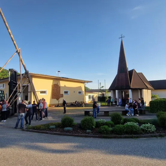 Eine Gruppe von Menschen versammelt sich um ein Gebäude mit einem Turm und einer Statue obenauf.