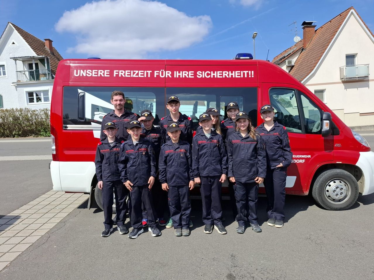 A group of young people dressed in navy blue uniforms stand in front of a red fire truck with text that says 'Our freedom for your safety.'