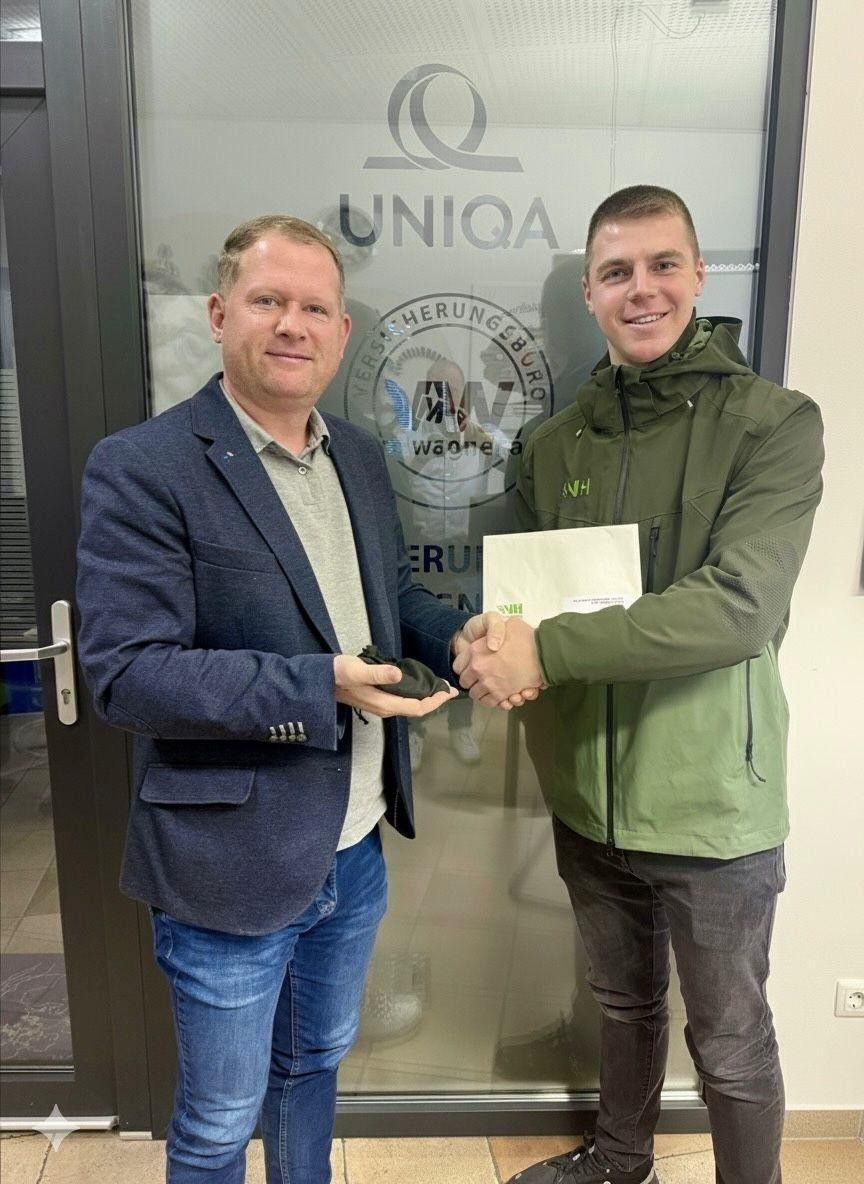 Zwei Männer stehen lächelnd vor einer Glastür. Der Mann auf der linken Seite hält ein Papier und ein schwarzes Objekt, während der Mann auf der rechten Seite ein Zertifikat in der Hand hat. Dahinter befindet sich eine Glasscheibe mit den Worten 'UNIKA' und 'Verbundgenossenschaft'.