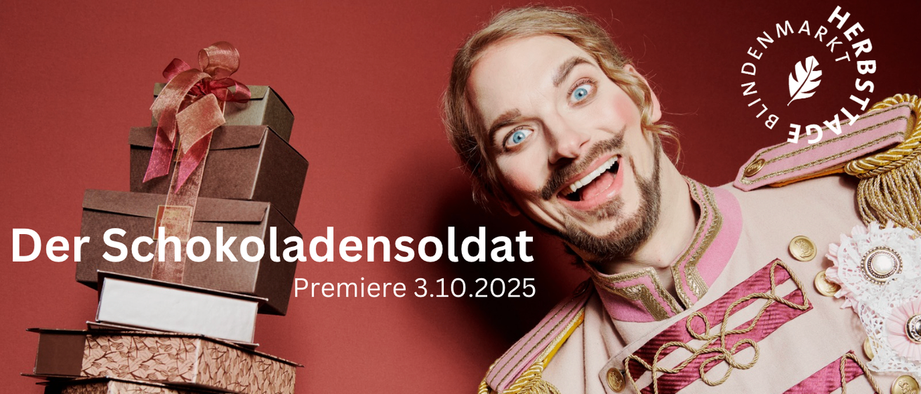 Ein Mann mit Bart und Schnurrbart lächelt vor einem roten Hintergrund für die Kamera. Er trägt ein pinkes und goldenes Uniform. Stapel von Kisten sind auf der linken Seite. Der Text lautet 'koladensoldat Premiere 3.10.2025'.