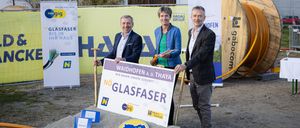 Drei Personen stehen vor einem Schild mit der Aufschrift Waidhofen. Die beiden Männer halten Schaufeln, und die Frau hält ein Bündel Drähte. Dahinter befindet sich ein Banner mit dem Text HAH und einem Logo.