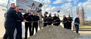 Gruppe von Menschen in formeller Kleidung mit Schaufeln am Bauplatz einer neuen Feuerwache. Ein großes Schild lautet Neubau Feuerwehrhaus Alt-Waidhofen Bauzeit: 2026-2027.