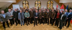 Eine Gruppe von Menschen in Uniformen und Anzügen, die für ein Foto in einem Raum mit Buntglasfenstern zusammenstehen.