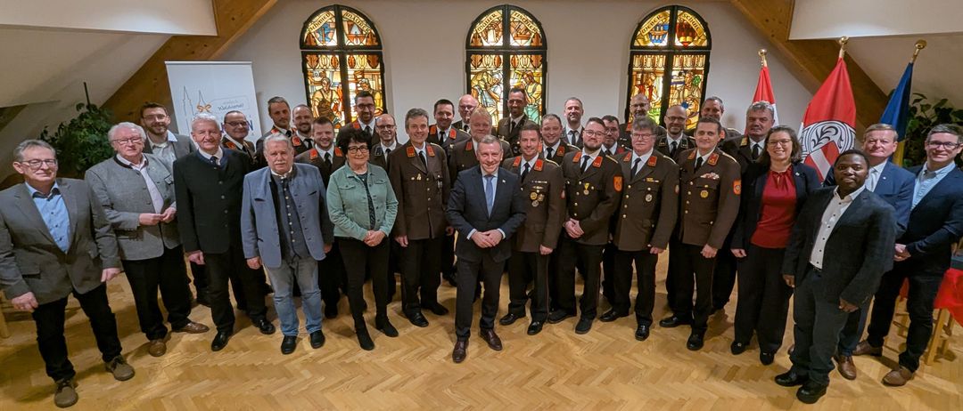 Eine Gruppe von Menschen in Uniformen und Anzügen, die für ein Foto in einem Raum mit Buntglasfenstern zusammenstehen.
