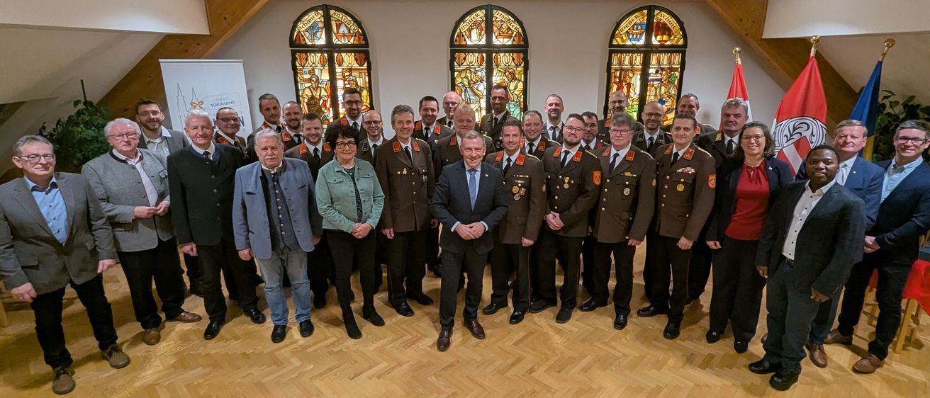 Eine Gruppe von Menschen in Uniformen und Anzügen, die für ein Foto in einem Raum mit Buntglasfenstern zusammenstehen.