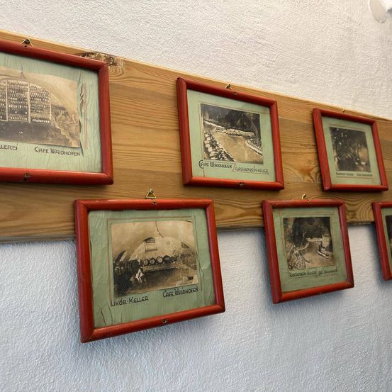 Eine Reihe rot gerahmter Bilder an einer Holzwand. Die Bilder haben verschiedene Szenen und sind mit ihren Namen beschriftet.