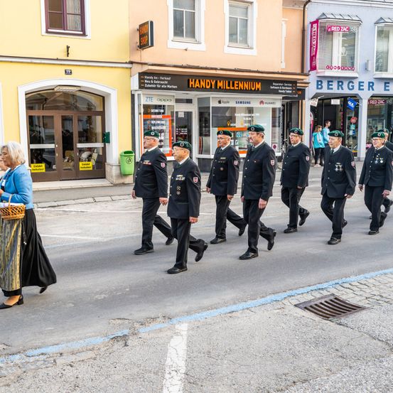 Veteranen in Uniform marschieren eine Stadtstraße hinunter, eine Frau geht auf dem Bürgersteig.