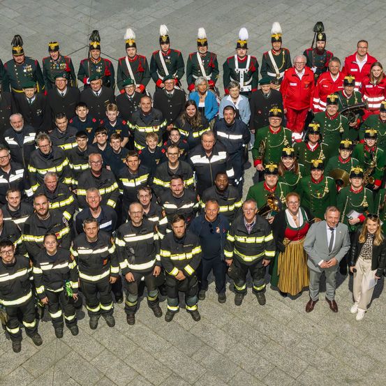 Eine Gruppe von Menschen in verschiedenen Uniformen, einschließlich Feuerwehrleuten und Militärkleidung, posiert für ein Foto auf einer gefliesten Oberfläche.