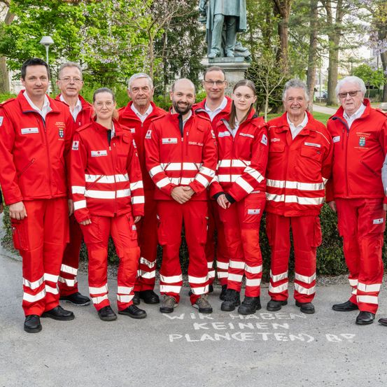 Eine Gruppe von Menschen in roten Uniformen mit weißen Streifen posiert für ein Foto vor einer Statue.