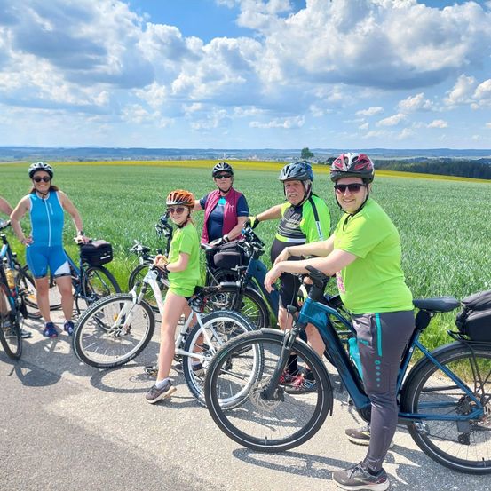 Eine Gruppe von Radfahrern in grünen Shirts steht auf einem Feld. Sie tragen Helme und Sonnenbrillen.