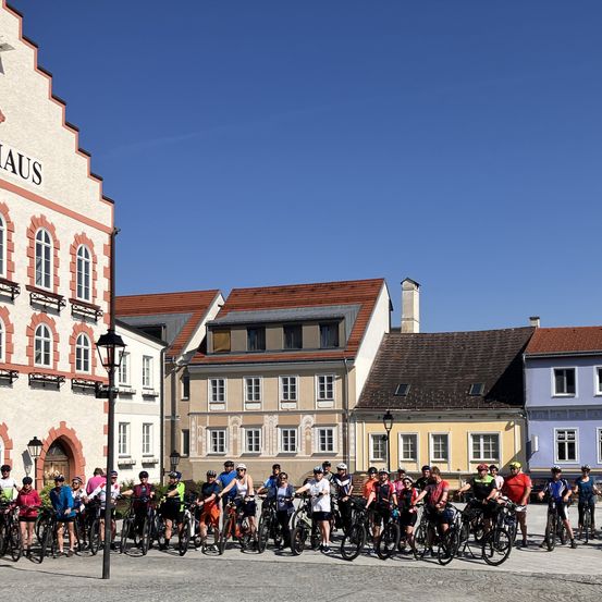 Eine Gruppe von Radfahrern steht an einem sonnigen Tag vor Gebäuden. Die Gebäude haben verschiedene Farben und Designs und einige haben Lampen.