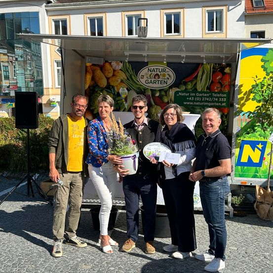 Fünf Personen stehen vor einem Food-Truck, zwei von ihnen halten eine Pflanze und eine Plakette, wahrscheinlich für ein Foto. Dahinter steht ein Lautsprecher auf einem Stativ.