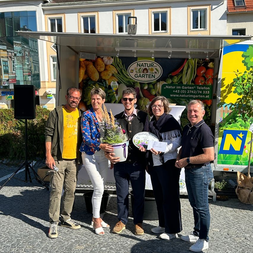 Fünf Personen stehen vor einem Food-Truck, zwei von ihnen halten eine Pflanze und eine Plakette, wahrscheinlich für ein Foto. Dahinter steht ein Lautsprecher auf einem Stativ.