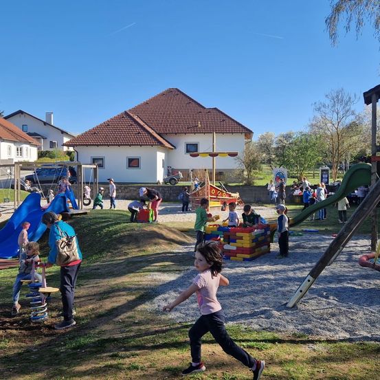 Ein Spielplatz mit verschiedenen Aktivitäten für Kinder. Ein Kind läuft, während andere auf Rutschen, Schaukeln und einem Piratenschiff spielen.