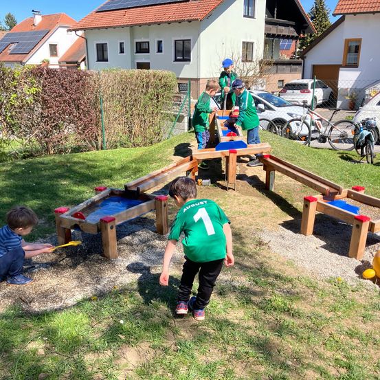 Mehrere Kinder spielen mit einem Holzspiel auf einem Kiesweg. Ein Kind rennt zum Spiel. Die Häuser im Hintergrund haben Solarpanele.