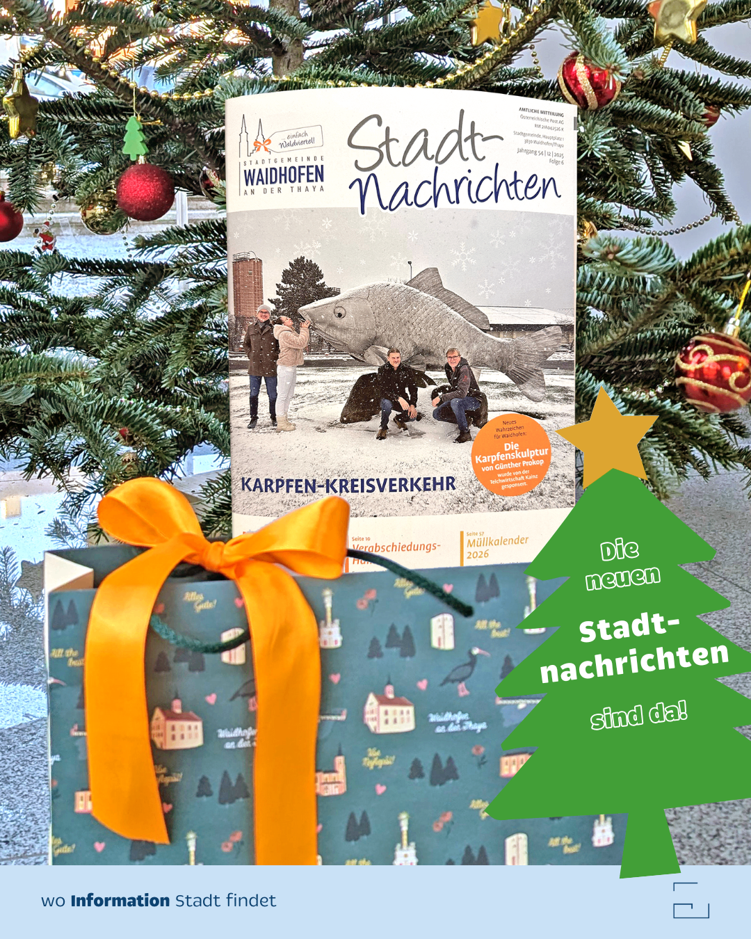 Eine Geschenkbox mit einer Schleife enthält eine Zeitschrift 'Stadt-Nachrichten' auf einem Weihnachtsbaum. Das Cover zeigt einen Fisch und Menschen in einer verschneiten Umgebung.