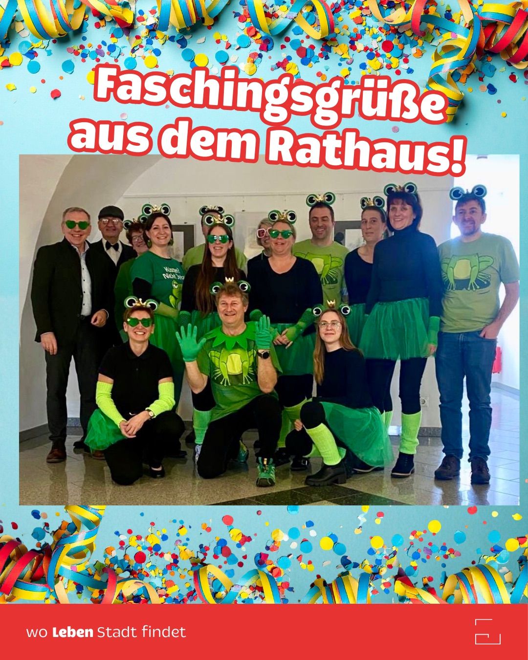 Group of people dressed in green frog costumes posing for a photo at the city hall with colorful confetti and decorations.