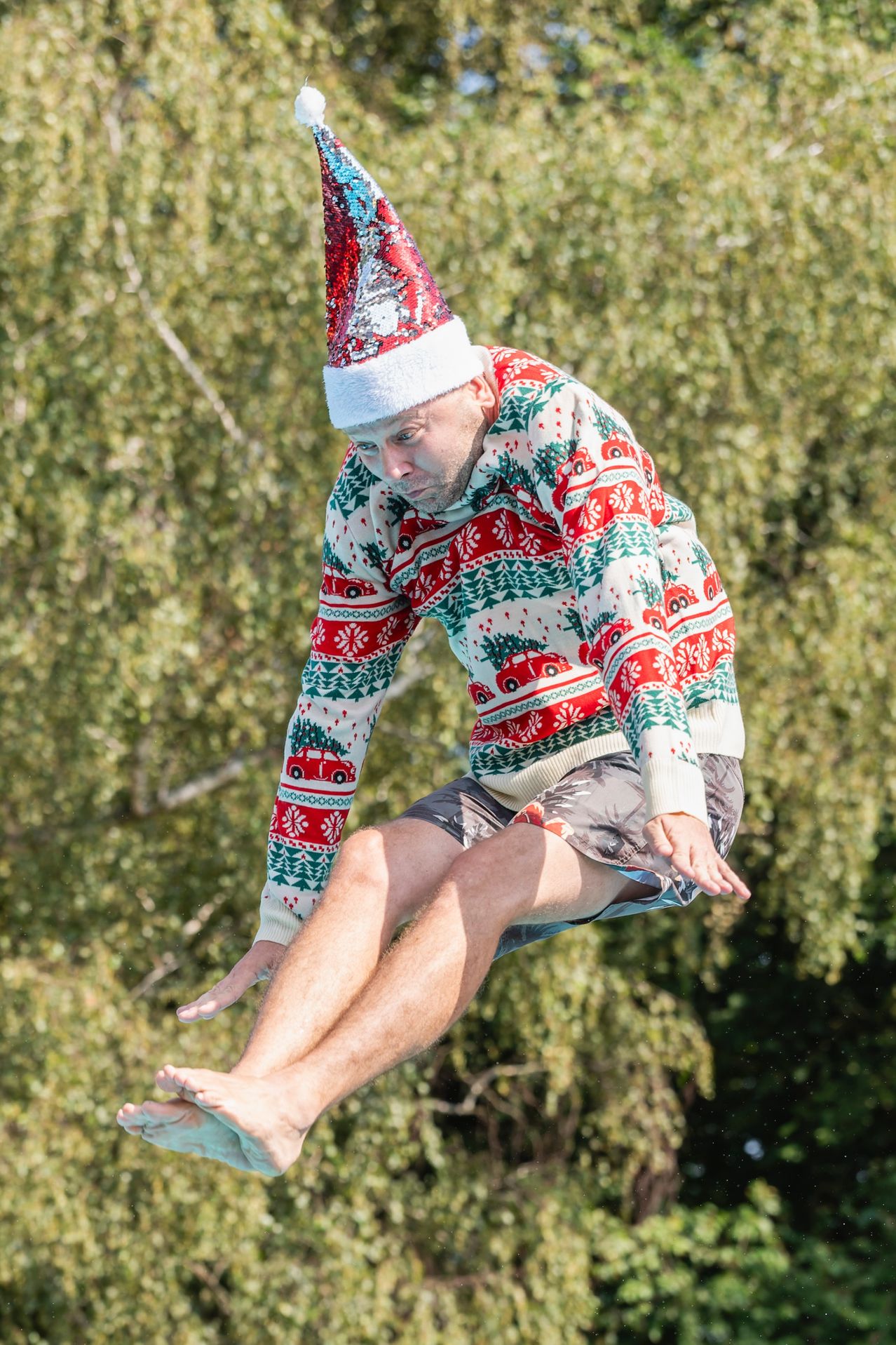 Ein Mann in einem Weihnachtspullover und Hut springt in ein Gewässer.