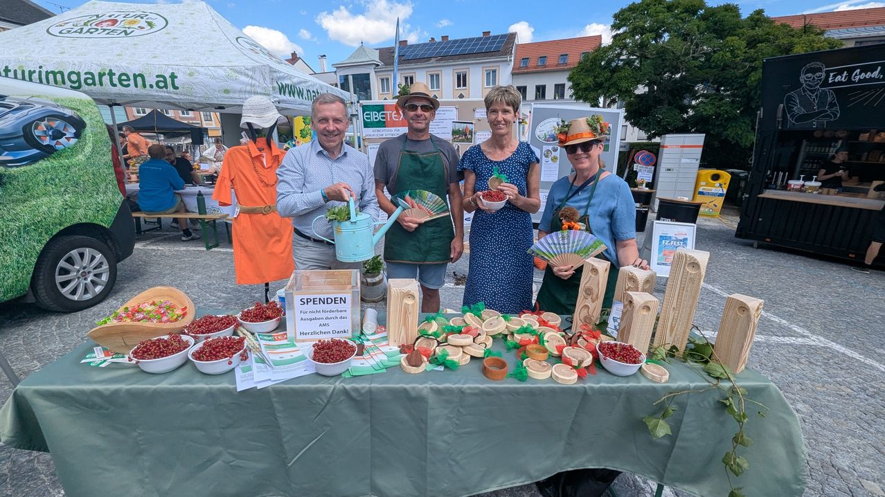 Vier Personen mit Spendenbox und roten Johannisbeeren auf einem Marktstand in Österreich