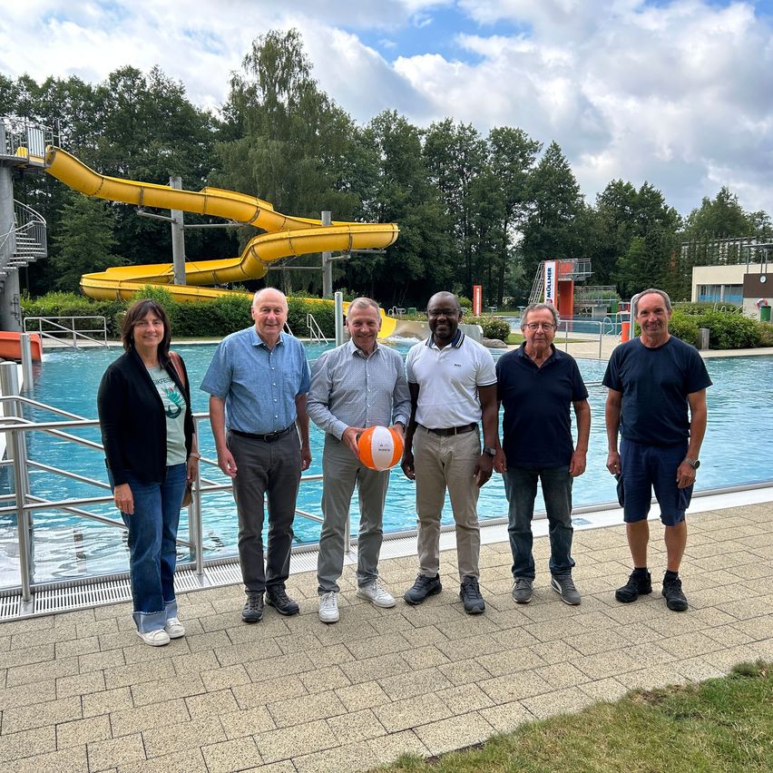 Schwimmbad-Besuch: Sechs Personen stehen vor einem Schwimmbecken mit gelber Wasserrutsche.