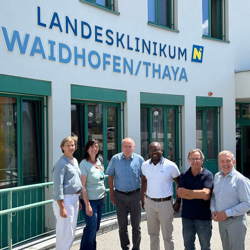 Fünf Personen stehen vor einem weißen Gebäude mit blauem Text. Das Gebäude ist das Landesklinikum Waidhofen/Thaya.