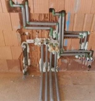 Offene Rohre und Armaturen an einer Holzwand, einige sind mit Isoliermaterial umwickelt.