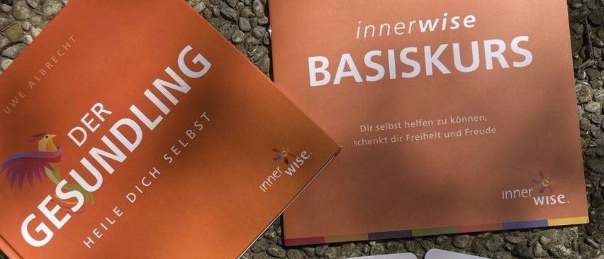 Ein Bild zeigt zwei Bücher und sechs Karten auf einer kiesigen Oberfläche. Die Bücher sind mit 'Der Gesundling' und 'innerwise BASISKURS' beschriftet. Die Karten sind mit 'Ja' und verschiedenen Themen wie 'Ernährung', 'Veränderung', 'Leben', 'Liebe', 'mir' und 'Erleichterung' beschriftet.