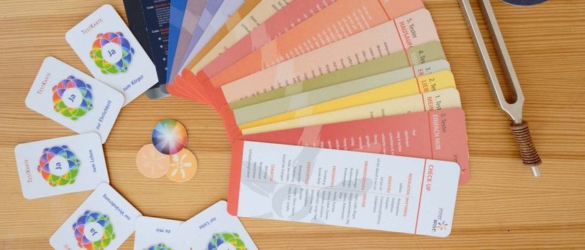 Eine Sammlung bunter Lesezeichen und Karten ist auf einer Holzoberfläche angeordnet. Die Lesezeichen sind mit Nummern und Titeln beschriftet. Verschiedene Karten mit unterschiedlichen Designs und Texten sind verstreut.